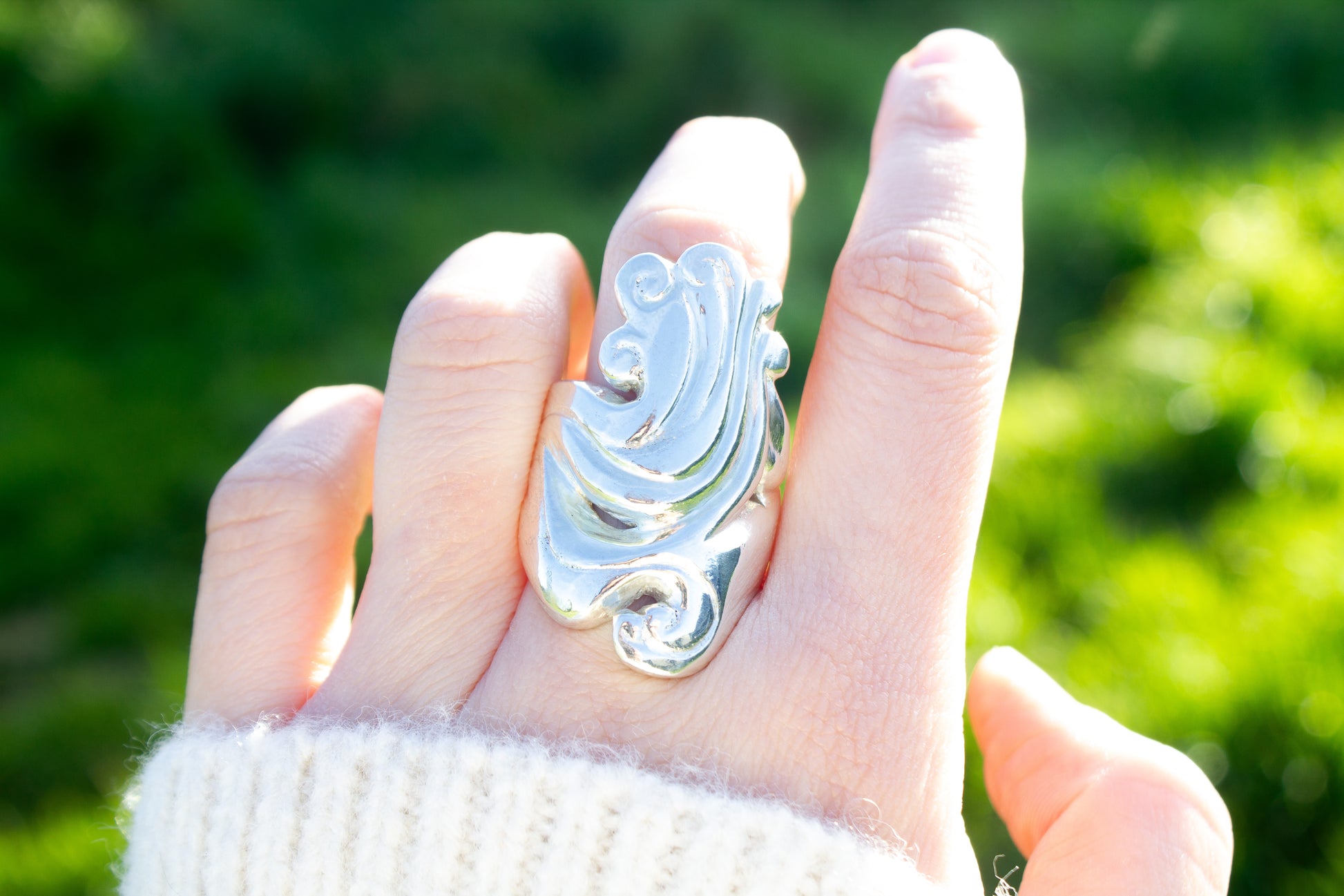 Lost wax cast sterling silver sculptural ring handmade in Ireland worn on the middle finger on a green background